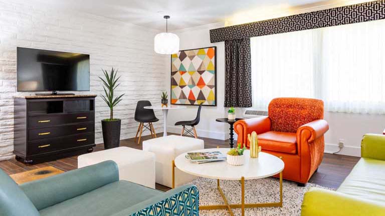 Hotel living room with orange, ivory, and teal furniture with bright natural light